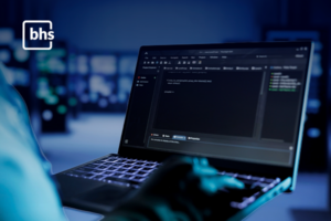 Especialista em TI analisando código e métricas de serviços gerenciados de TI em um laptop, representando a proatividade e segurança da BHS.